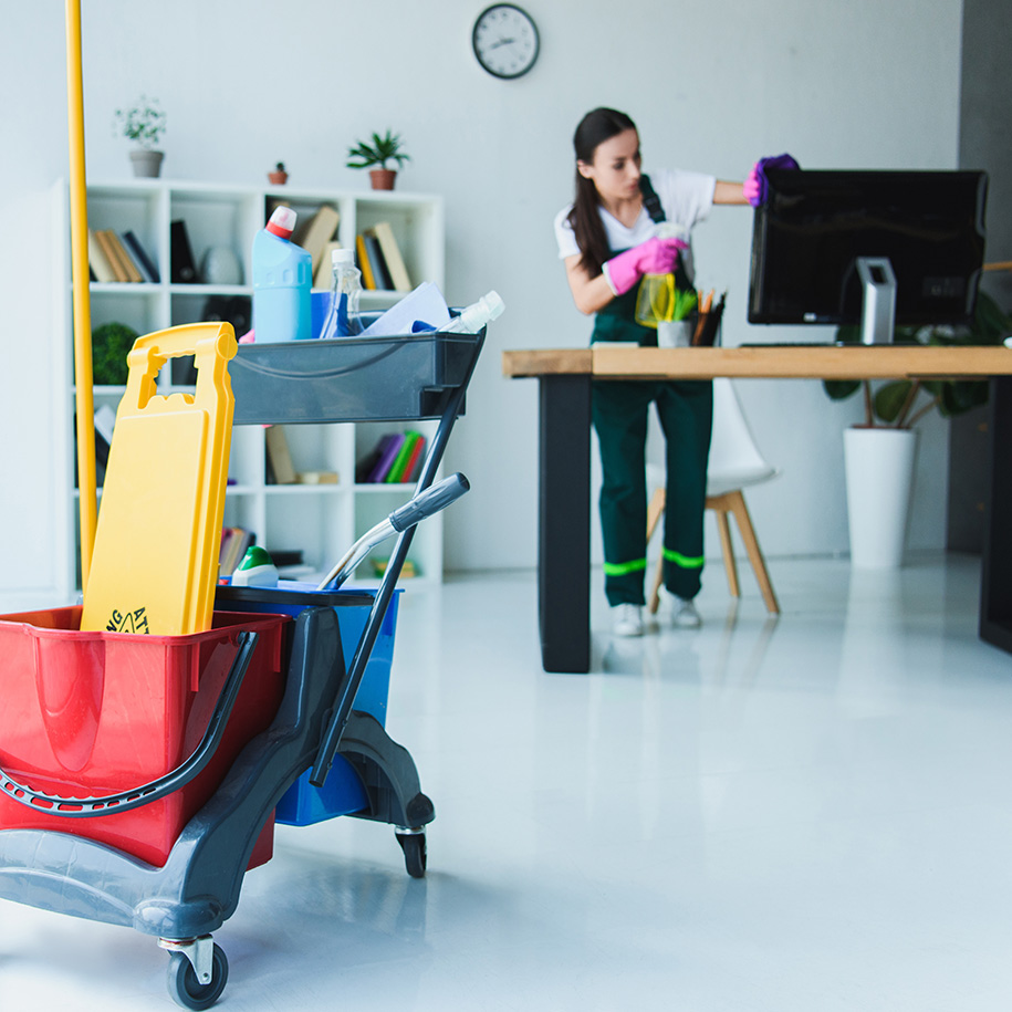young female janitor cleaning office with various cleaning equipment